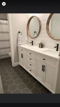 a bathroom with two round mirrors above the sinks and white cabinets, along with gray tile flooring