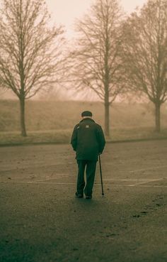 a man walking down the street with a cane in his hand and trees behind him