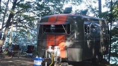 an orange and black bus parked in the woods next to water hoses with trees behind it