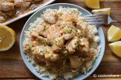 a plate of chicken and rice with lemon wedges on the side next to it