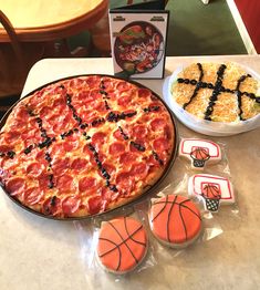 a pizza with pepperoni and black olives next to some basketball cookies on a table