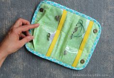 a hand is holding an open green and yellow purse with buttons on it, which are attached to the side of the bag