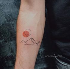 a person with a small tattoo on their arm that has mountains and an orange sun