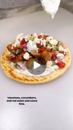 a flatbread pizza topped with tomatoes, cucumbers and feta on a white surface