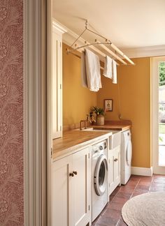 a washer and dryer in a small room with yellow walls, tile flooring and white cabinets