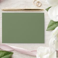 a notepad and pen on a table with white flowers, greenery and pink ribbon