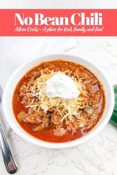 a white bowl filled with chili and sour cream on top of a table next to a green pepper shaker