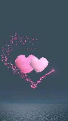 two heart shaped clouds floating in the air over water with pink confetti falling from them