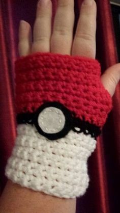 a hand wearing a red and white crocheted wristband with a pokeball on it