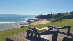 a woman laying on top of a wooden bench next to the ocean