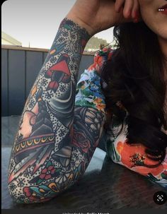 a woman sitting at a table with tattoos on her arm and arms behind her head