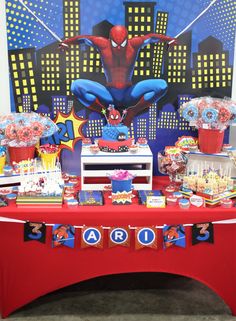 a red table topped with cake and cupcakes next to a spiderman backdrop