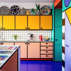 the kitchen is brightly colored and has art on the wall above the countertop, as well as colorful cupboards