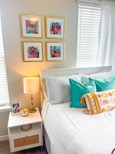 a white bed topped with lots of pillows next to a lamp and pictures on the wall