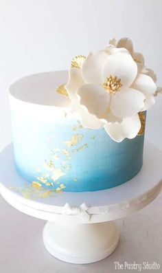 there is a blue and white cake with flowers on the top, sitting on a stand