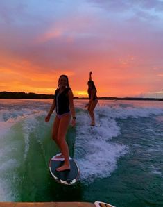 two women riding surfboards on top of a wave in the ocean at sunset or dawn