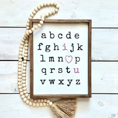 a cross - stitch alphabet with tassels and beads on a white wooden background