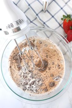 a glass bowl filled with batter next to a whisk and some strawberries