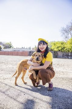 a woman kneeling down with a dog in her lap and wearing a yellow hat on top of her head