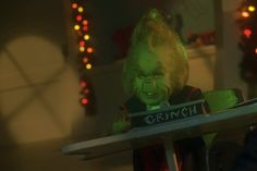 a creepy clown is sitting at a table with a sign on it that says grinch