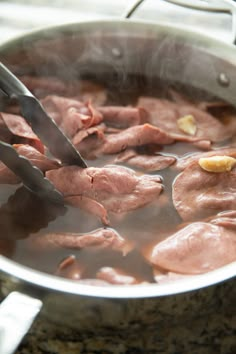 meat being cooked in a pot with tongs