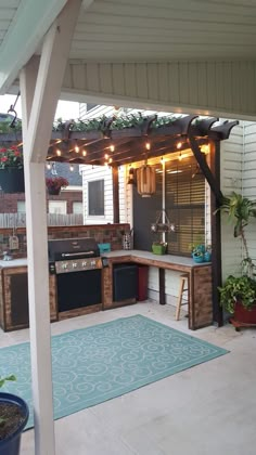 an outdoor kitchen with lights and potted plants on the outside wall, under a pergolated roof