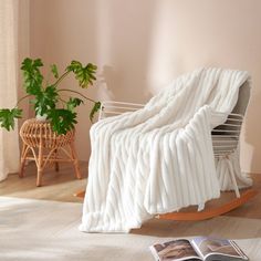 a white blanket sitting on top of a wooden rocking chair next to a potted plant