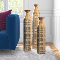 three gold vases sitting next to each other on a rug in front of a blue couch