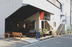 an outside view of a store with wooden benches and chairs on the side of the street