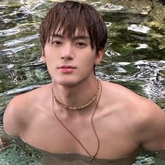 a young man in the water wearing a necklace and looking at the camera with an intense look on his face