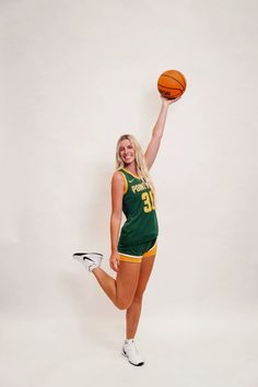 a woman holding a basketball in her right hand and posing for the camera with one leg up