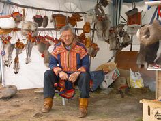 an older man sitting in front of a display of deer heads and other animal hangings