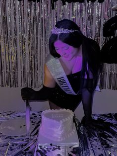 a woman wearing a tiara cutting a cake with a knife in front of her