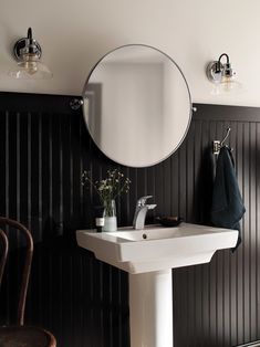 a white sink sitting under a round mirror next to a wall mounted faucet