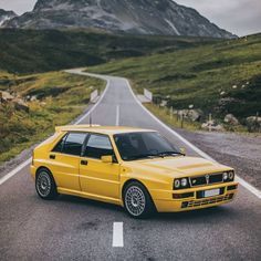 a yellow car is parked on the side of the road in front of some mountains