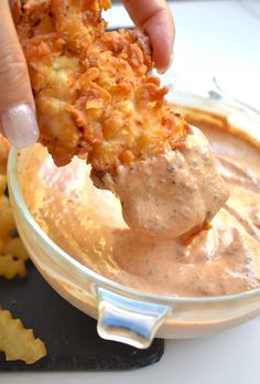 a person dipping some kind of food in a bowl with dip and chips on the side