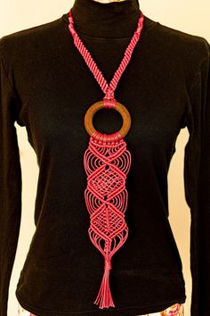 a woman wearing a black shirt and pink necklace with a wooden circle hanging from it