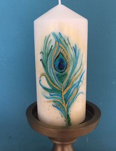 a white candle with a blue and green peacock feather painted on it's side