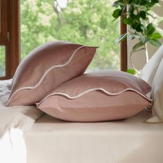 two pink pillows sitting on top of a white bed next to a potted plant