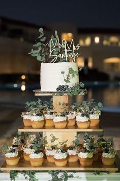 a cake and cupcakes on a table with greenery