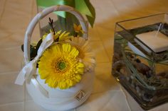 a white basket with yellow flowers in it next to a candle and some rocks on the table