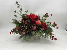 a vase filled with red flowers and greenery on top of a white tablecloth