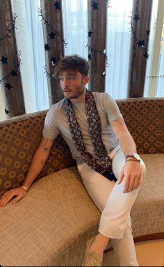 a man sitting on top of a couch in front of a window wearing white pants