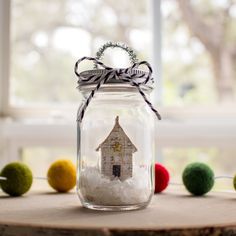 a glass jar filled with white snow and a house on the inside, surrounded by pom - poms