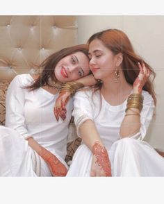 two beautiful young women sitting next to each other on top of a bed with their arms around each other