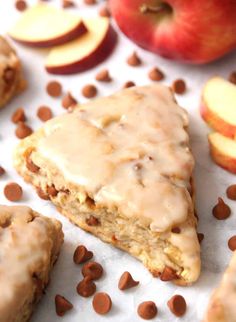 there is a piece of cake with icing and chocolate chips on the table next to apples