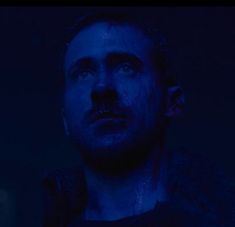 a man in the dark looking at something with blue light on his face and chest