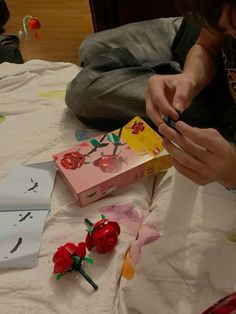 a person sitting on a bed holding a cell phone next to two boxes and flowers