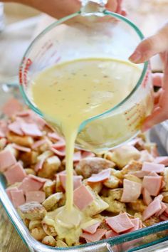 someone pours dressing into a casserole dish with ham and potatoes in it