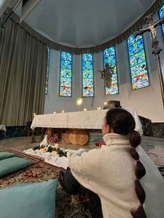 a woman sitting on the floor in front of a altar with stained glass windows behind her